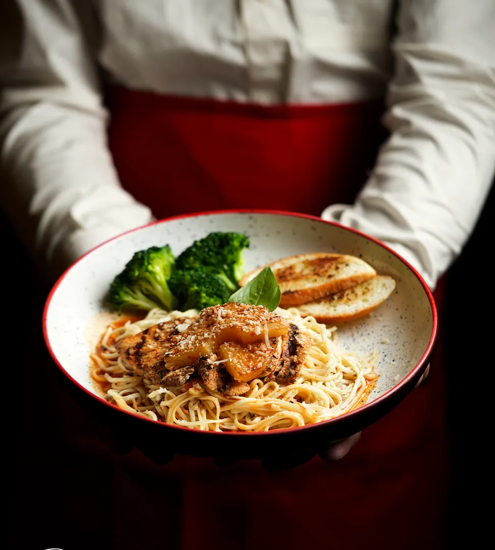 A server in a red apron presenting a bowl of pasta