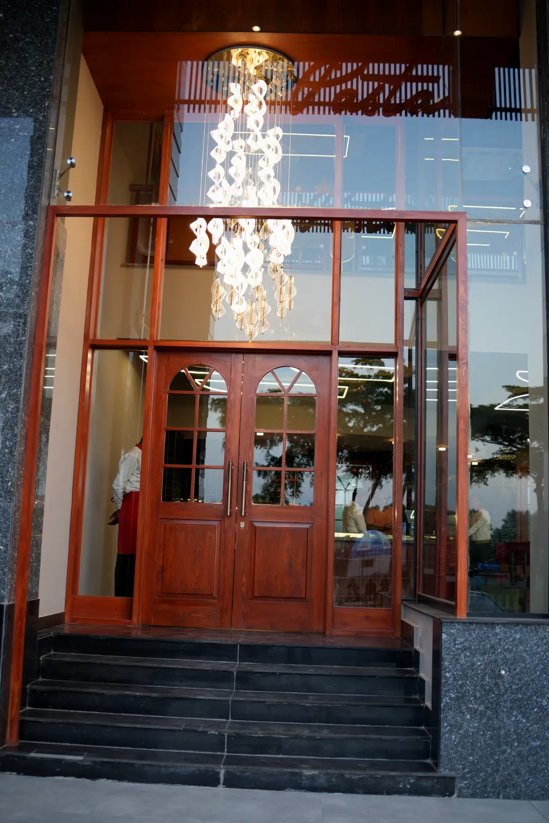 The entrance to Pasta La Vie in Falcon Downtown, with arched wooden doors and the chandelier glowing through the glass