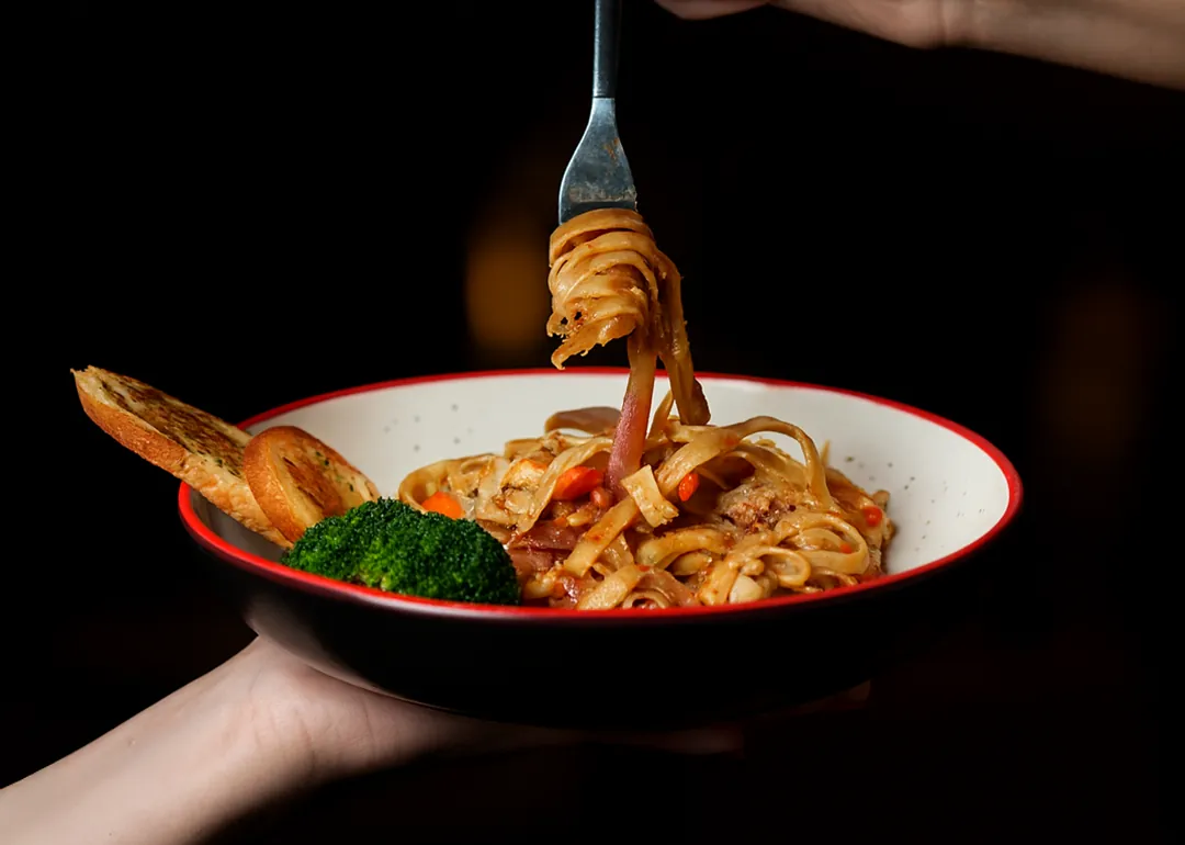 Pasta twirled on a fork above a red-rimmed bowl